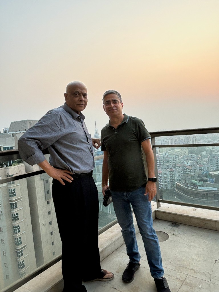 Ashok Anand dusk में city देखते हुए balcony पर खड़े